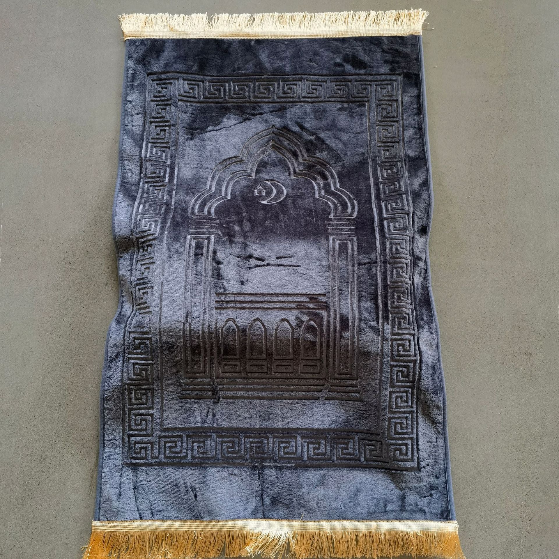 Blue prayer rug with intricate design and gold fringes on a plain background