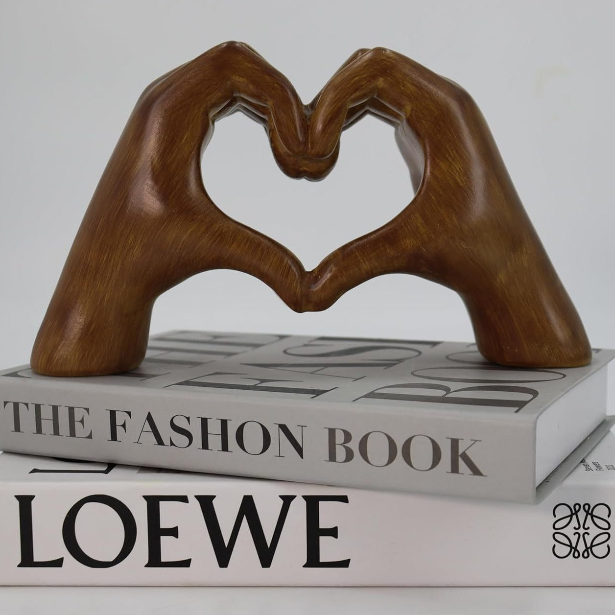 Wooden sculpture of hands forming a heart shape on top of a LOEWE book.