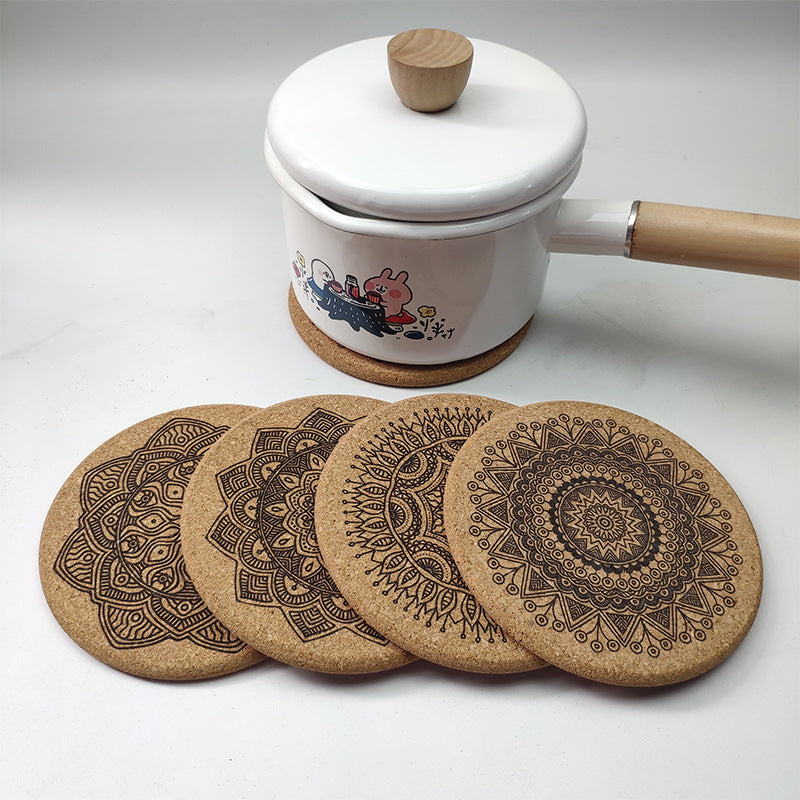 Set of cork coasters with intricate designs in front of a white pot with a wooden handle.