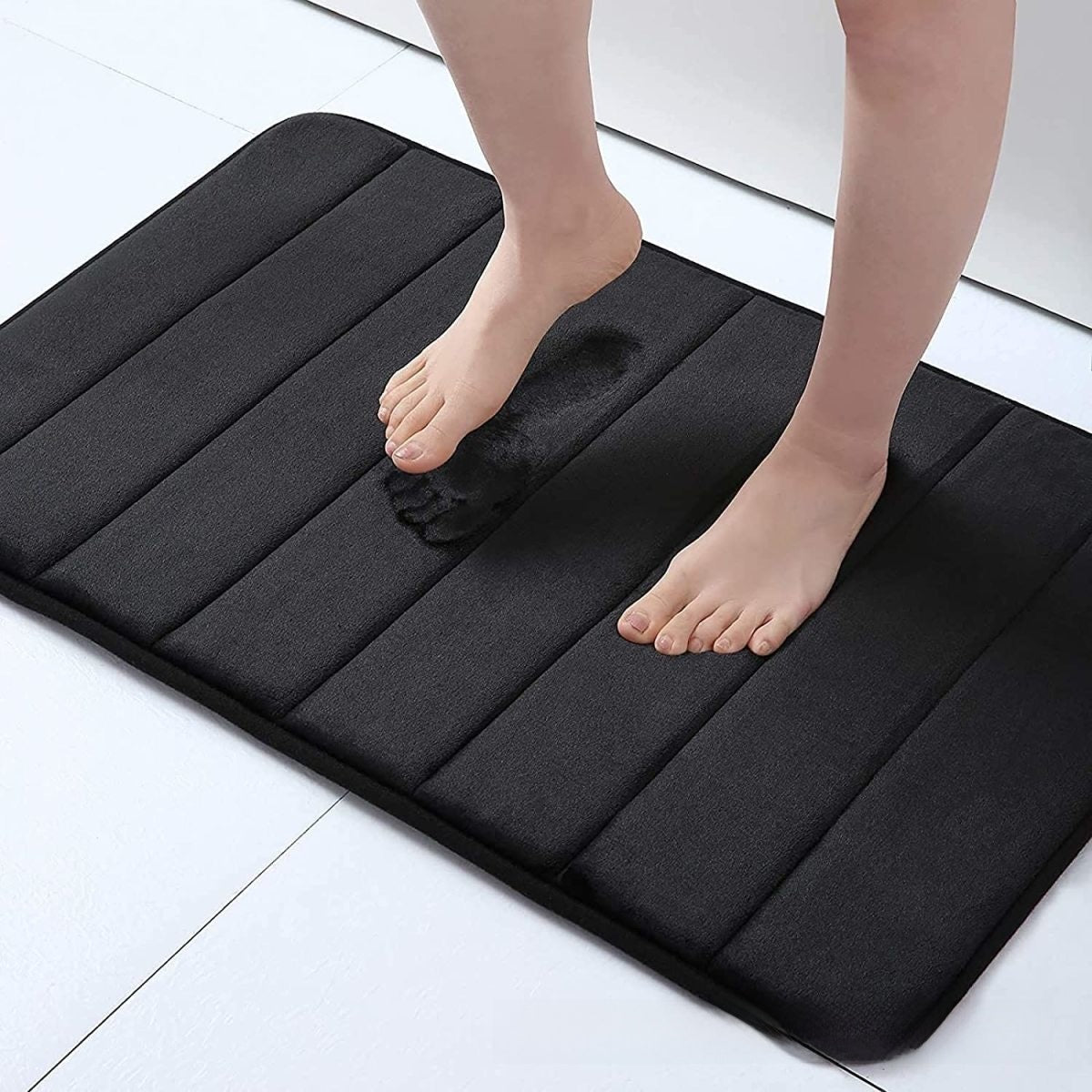 Black cushioned mat with feet stepping onto it on a light-colored floor.