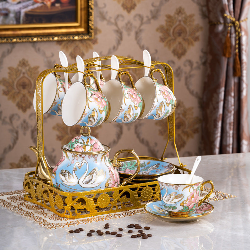 Set of ceramic tea cups and saucers with gold accents on a decorative stand, placed on a table with a patterned background.
