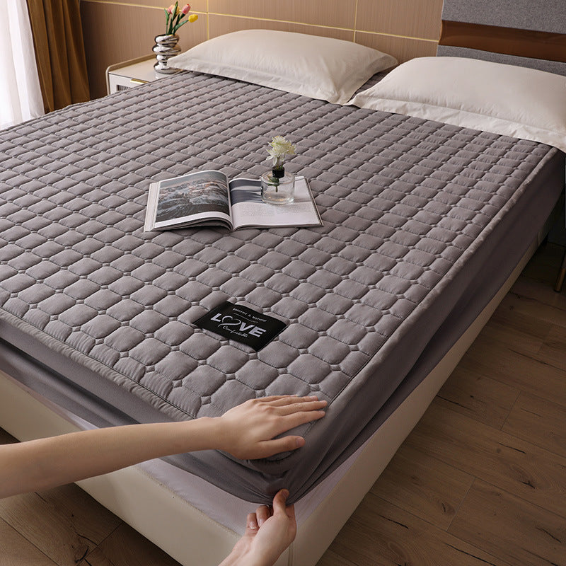 Gray quilted mattress cover on a bed with a hand adjusting it, in a bedroom setting.