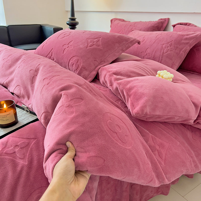 Pink textured comforter and pillows on a bed with a candle and remote control in the background.