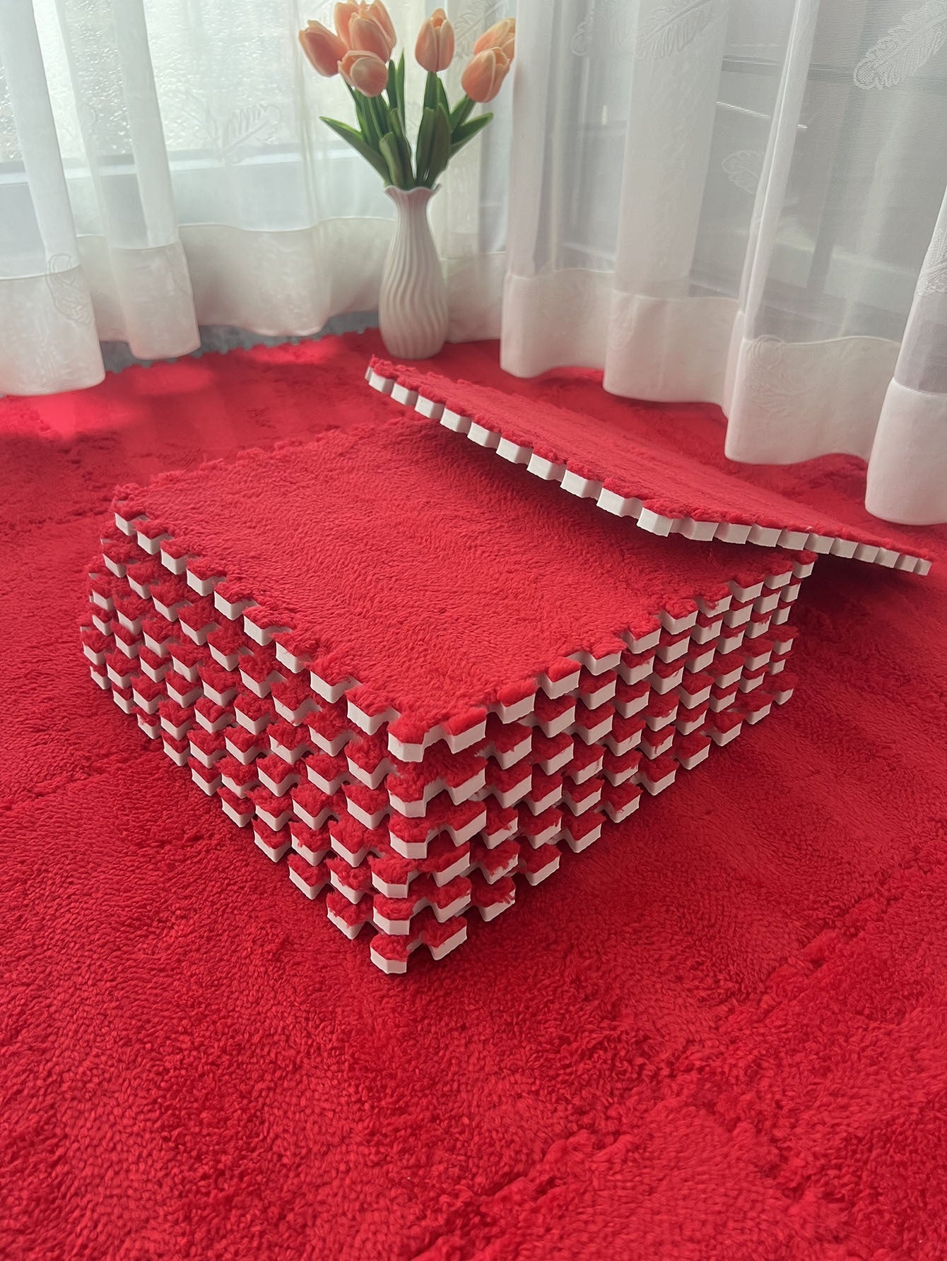 Red foam puzzle mat on a red carpet with a vase of tulips in the background.