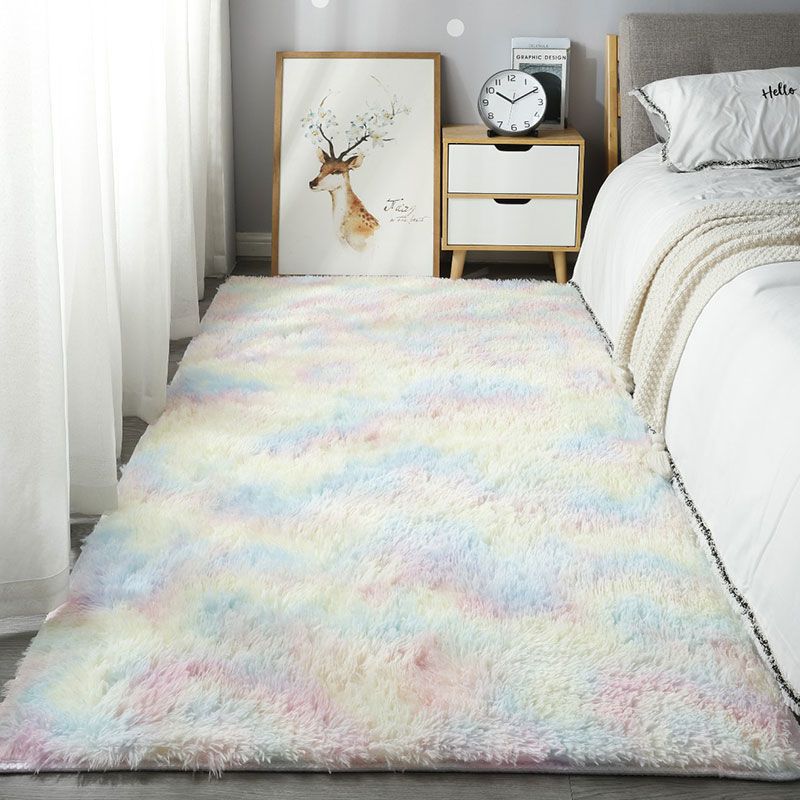 Multicolored rug on a bedroom floor with a bed and nightstand in the background.