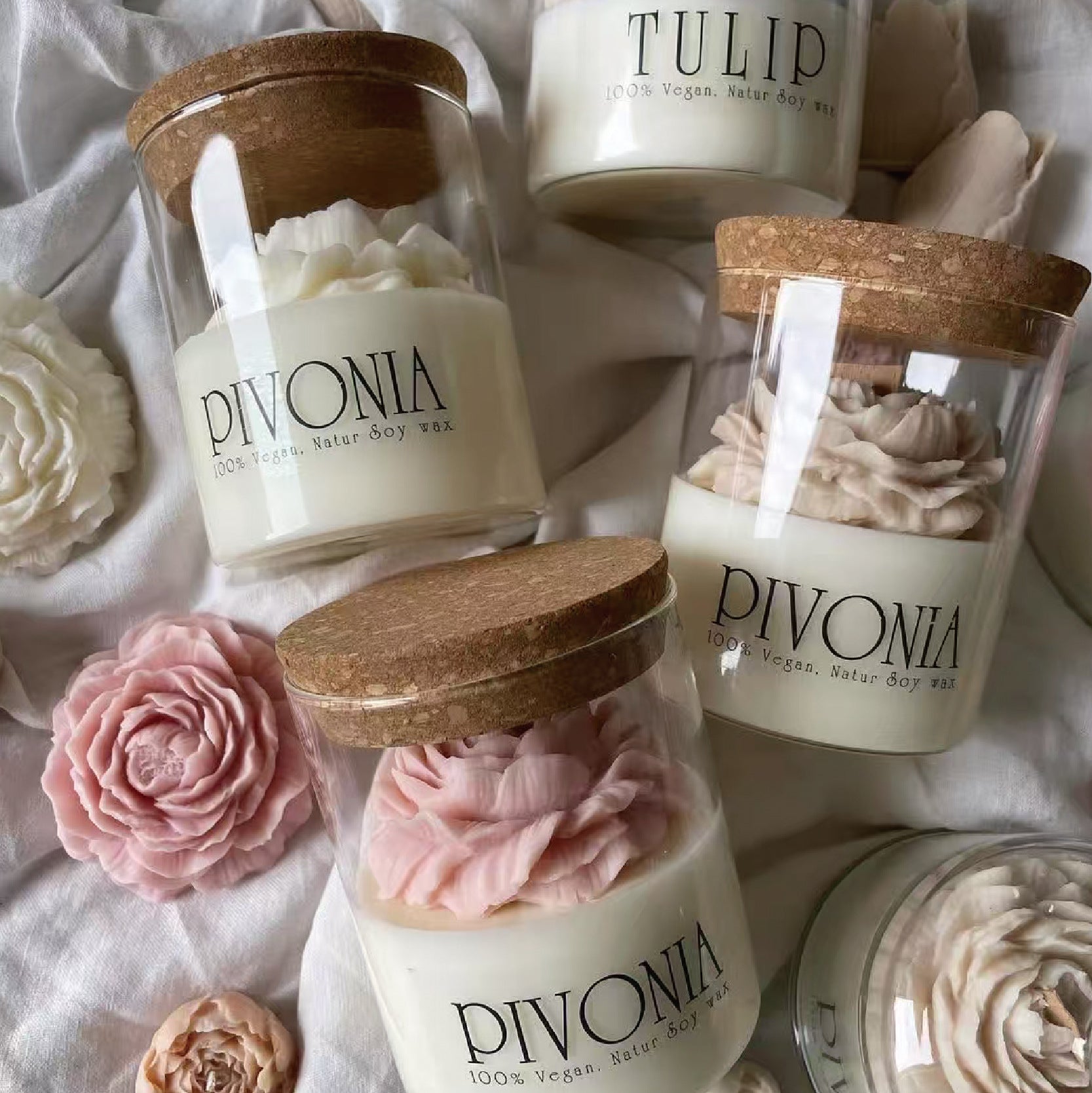 Candles with 'DIVONIA' and 'PIVONEA' branding on a soft fabric background.