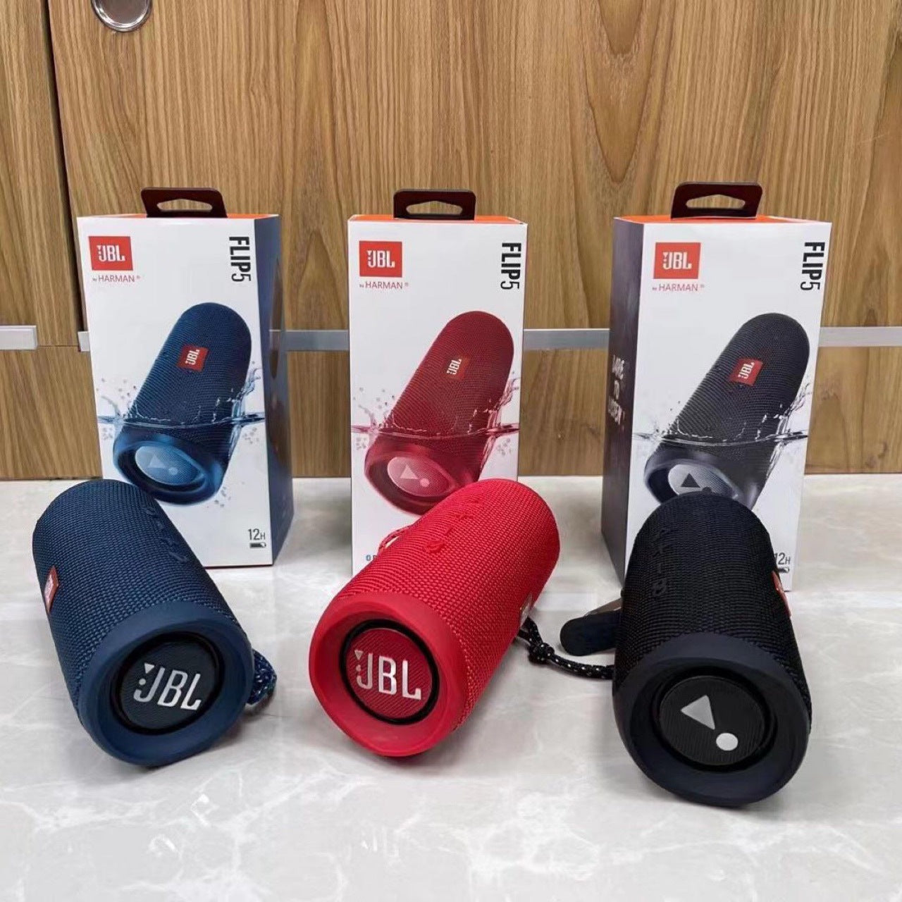 Three JBL Flip 5 speakers in blue, red, and black with their packaging on a white surface.