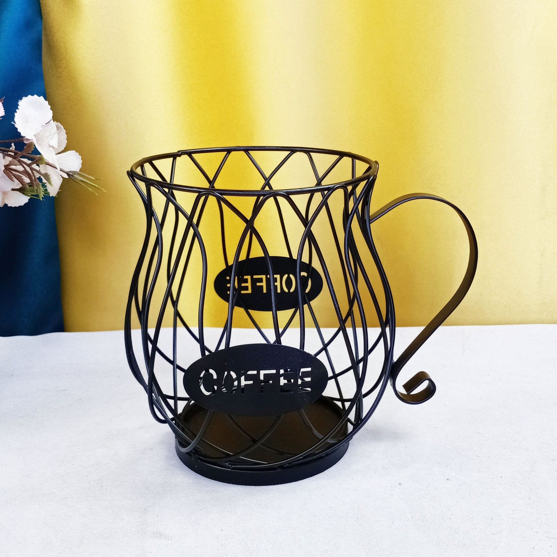 Black wire  coffee capsules basket with 'Cafetera' label on a white surface with yellow background